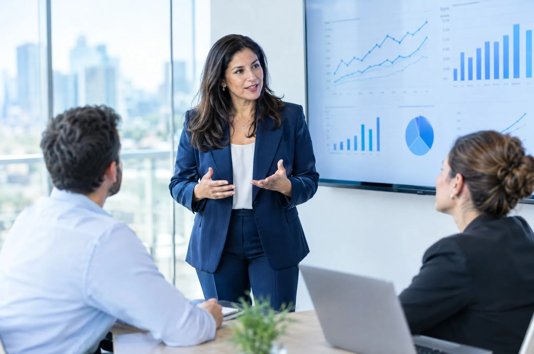 A company owner walks two colleagues through charts on a conference room display.