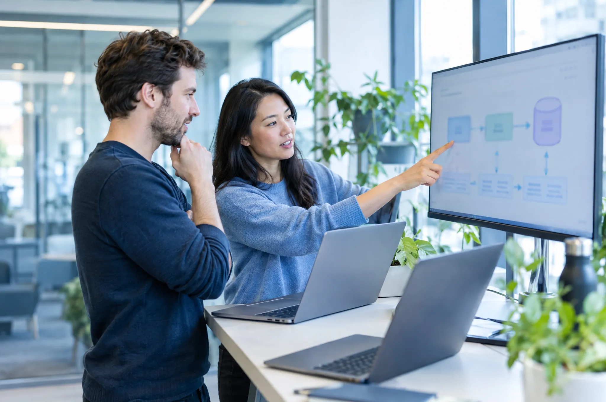 Two engineers discuss a system architecture diagram on a large monitor.